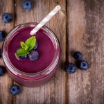 Blueberry smoothie in a glass jar with a straw and sprig of mint