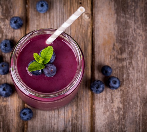Blueberry smoothie in a glass jar with a straw and sprig of mint